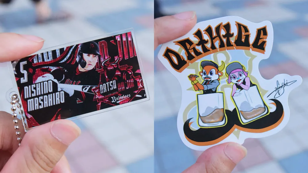 左のキーチェーンは光が当たるとホログラムが輝き、キラキラ。右は博志投手のイラストが素敵なステッカー ©PLM