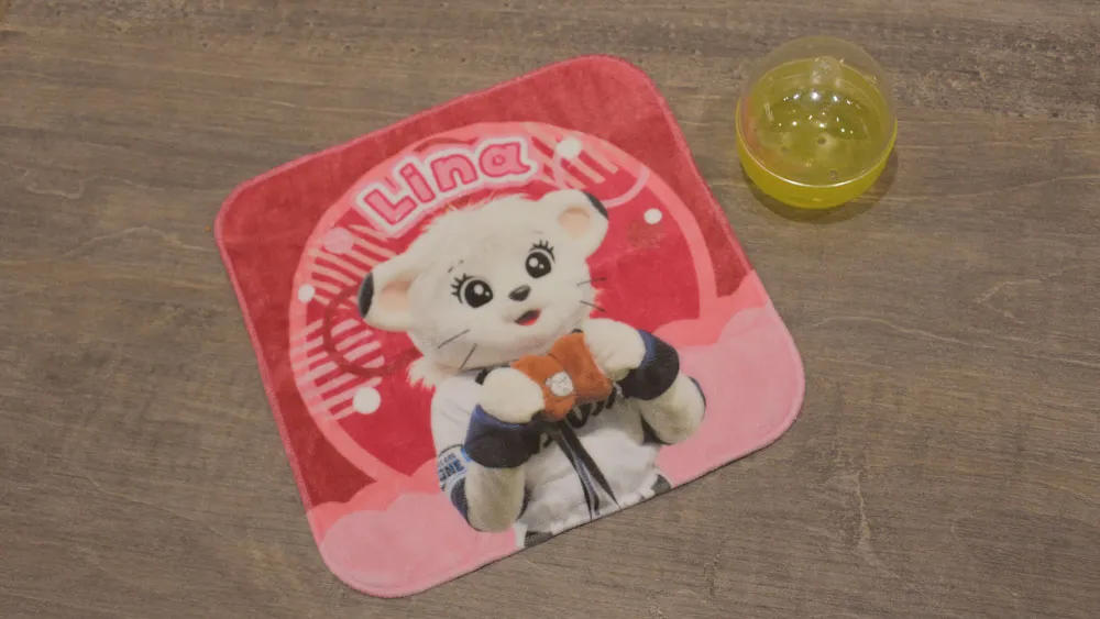 自身でプロデュースした『おにくパクパクポシェット』を持っているライナがデザインされたミニタオル ©PLM